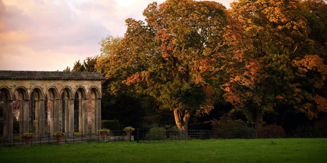 A view of the the stone arches of the Orangery with autumn leaves in the background.
